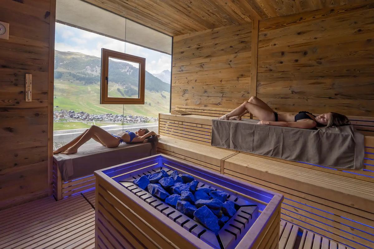 Koka sauna ar lielu logu uz zaļiem kalniem